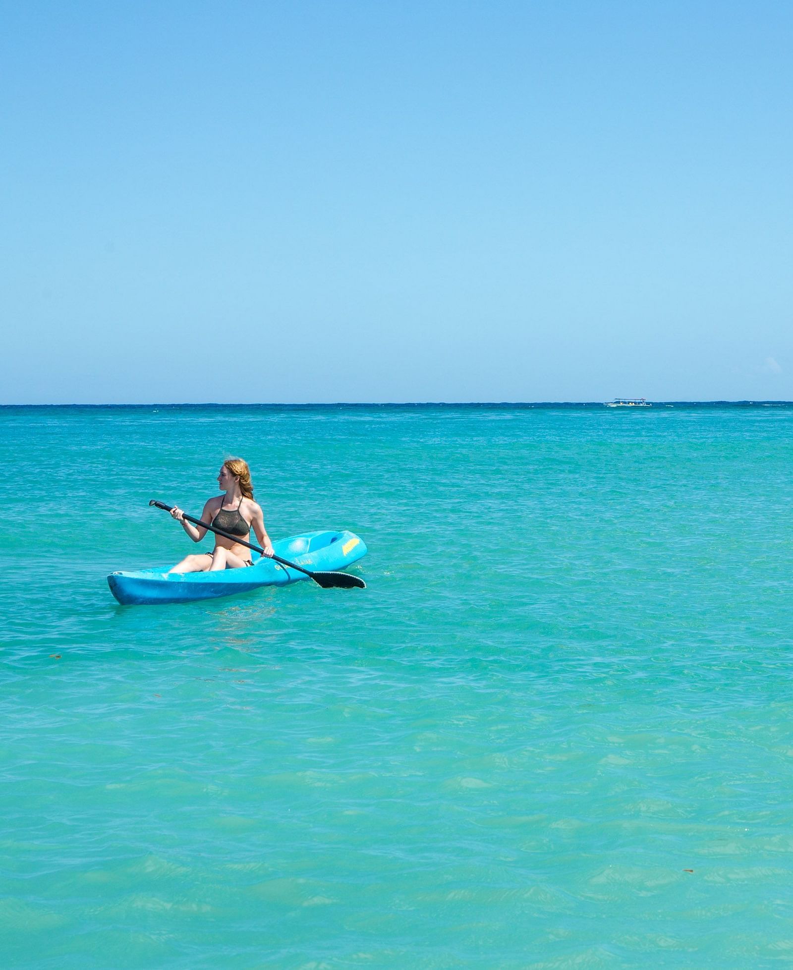 A person sitting on a paddleboard in the middle of clear blue waters, with a vast open horizon in the background | Abaco Inn