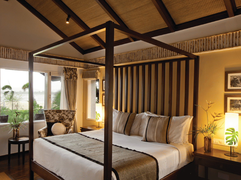 An overview of a bedroom with a four poster bed, side lamps and tables at one of the rooms at The Serai Kabini, ideal for Weekend Trips from Bangalore for Couples.
