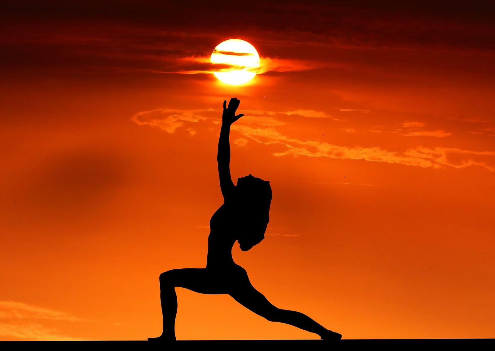A woman's silhouette seen while she is performing a yoga pose with the sun above her hands.