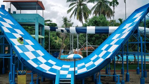 A thrilling blue-and-white checkered V-shaped water slide with a rider on a green tube enjoying the adventure at Black Thunder – Water Theme Park.