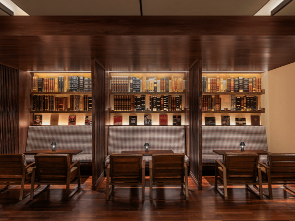 A cozy restaurant with wooden tables and chairs, and a wall lined with liquor bottles and books.