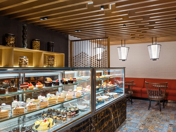A bakery display case filled with pastries, cakes, and other desserts, with a coffee machine in the background.