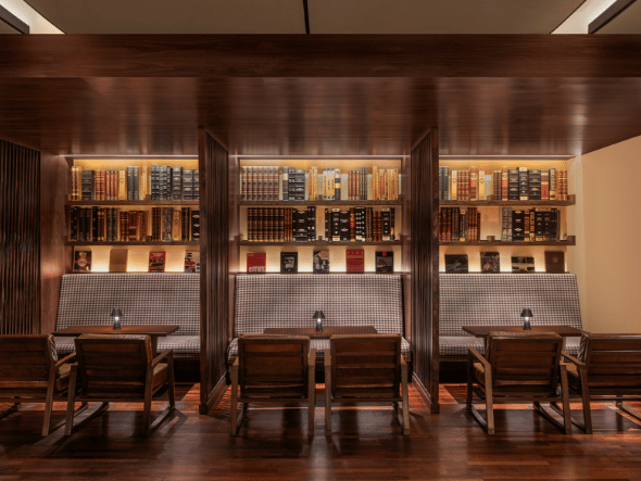 A cozy restaurant with wooden tables and chairs, and a wall lined with liquor bottles and books.