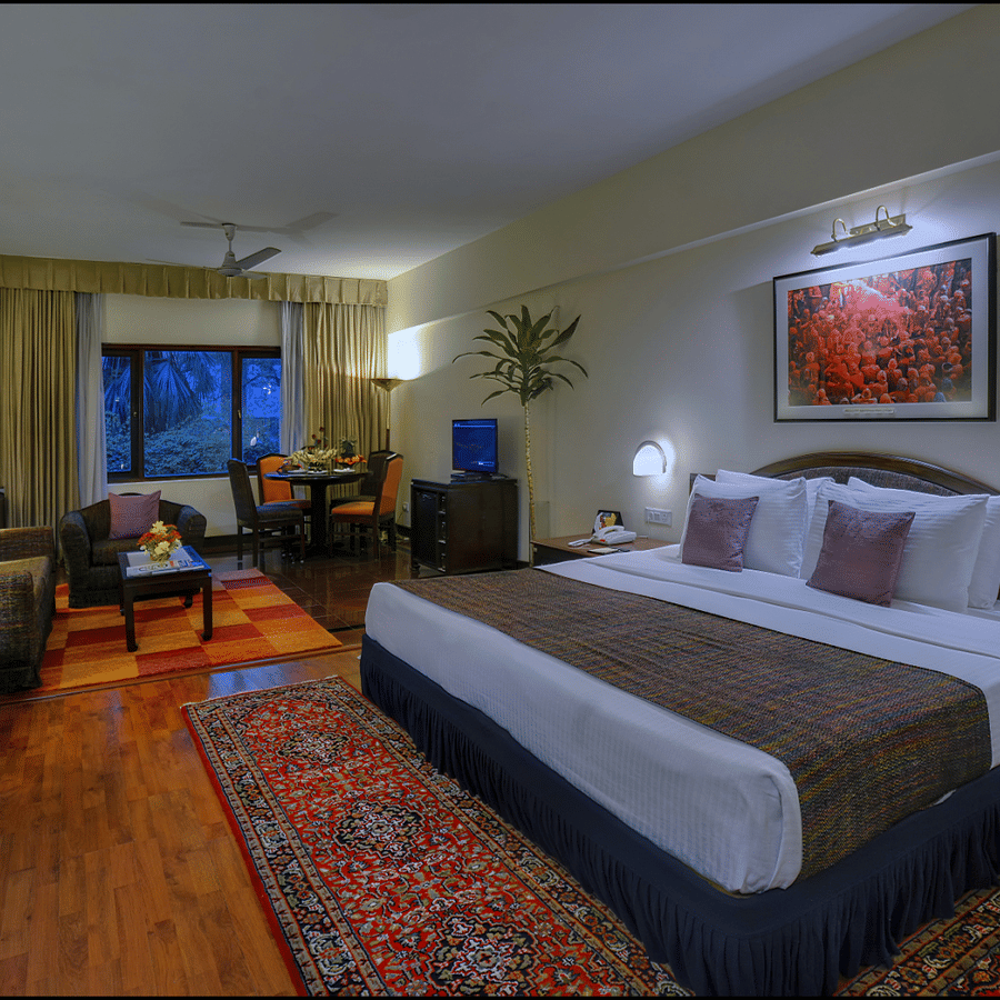 A Junior Suite at The Clarks Varanasi featuring a neatly-made bed, a patterned carpet, wooden furniture and a seating area.