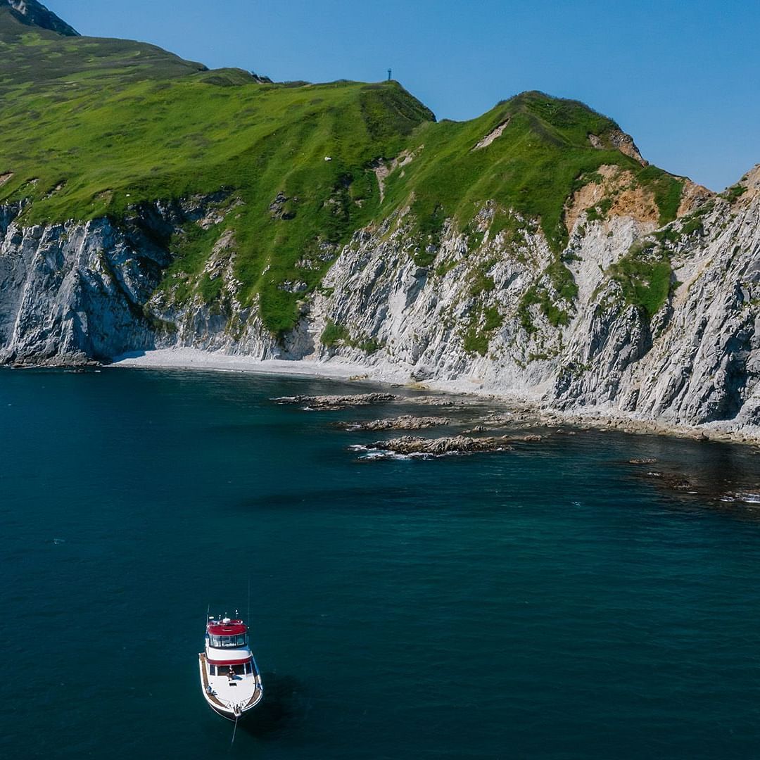 An image of a boat in a deep blue sea and green mountains in the background