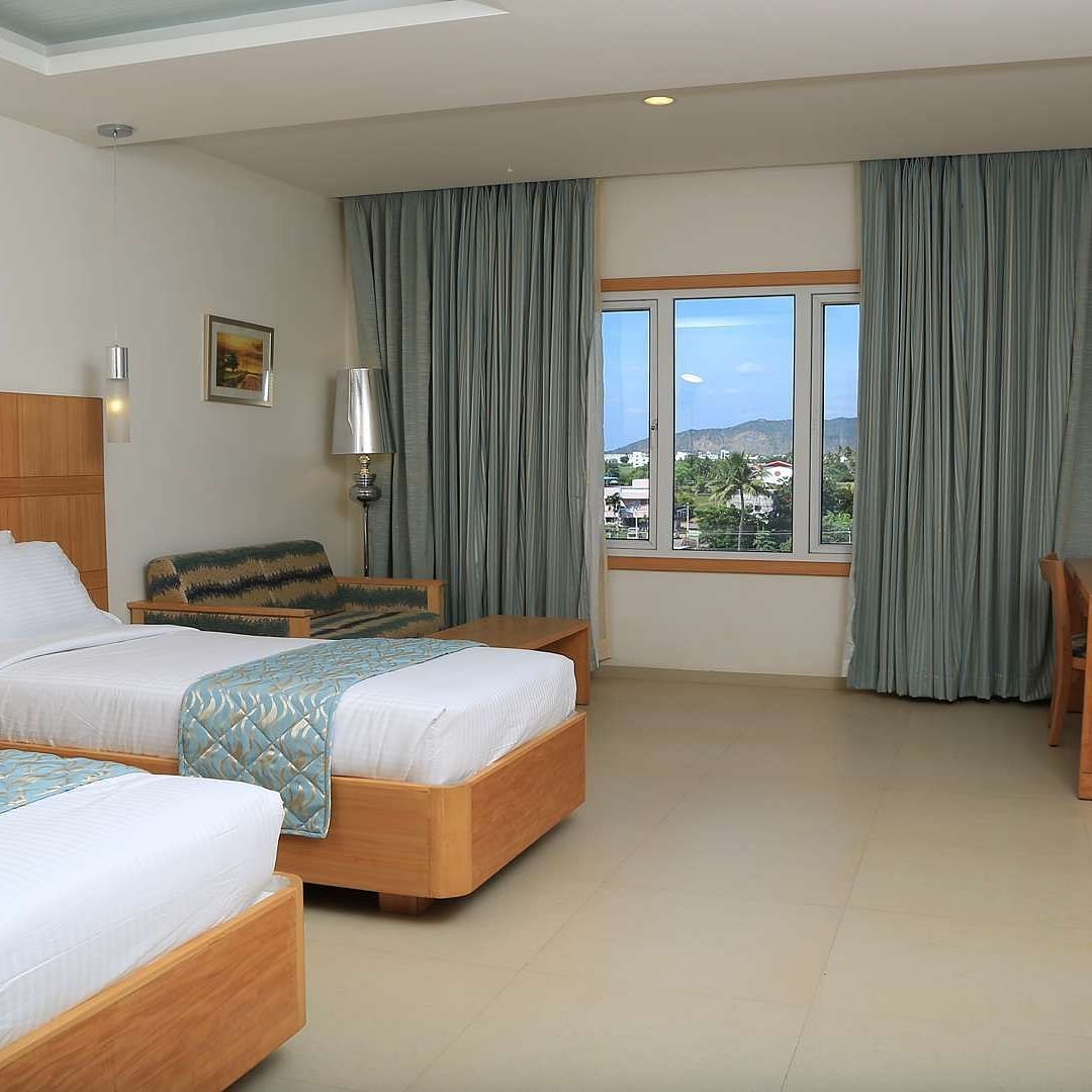 A spacious twin-bedroom setup with a contemporary design, large windows, and modern amenities.- Dhanalakshmi Srinivasan Hotels, Perambalur