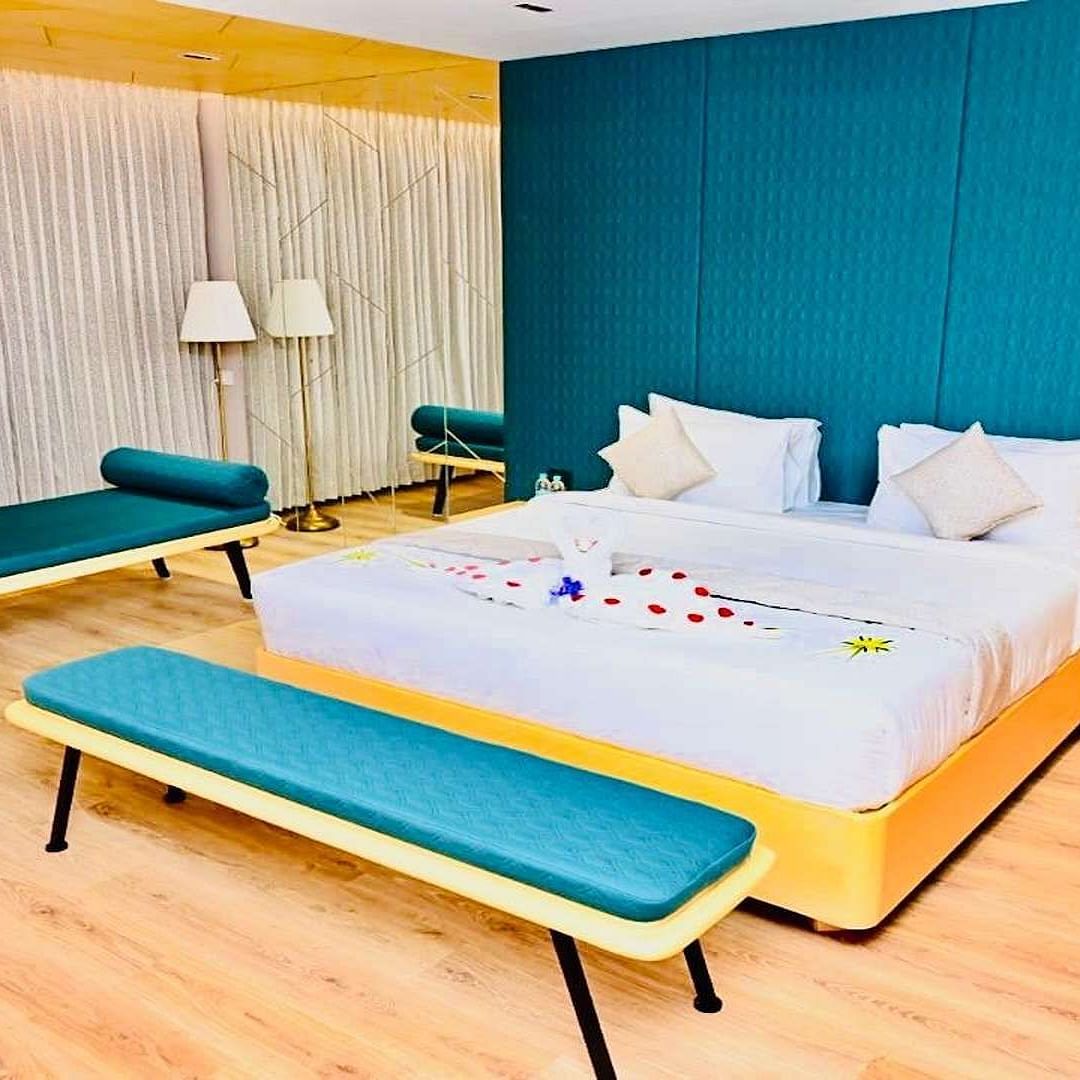 Close up view of a Presedential Suite featuring a King size bed with white linens and decorative swans, a green accent wall, yellow furniture, and hardwood floors - Dhanalakshmi Srinivasan Hotels, Perambalur