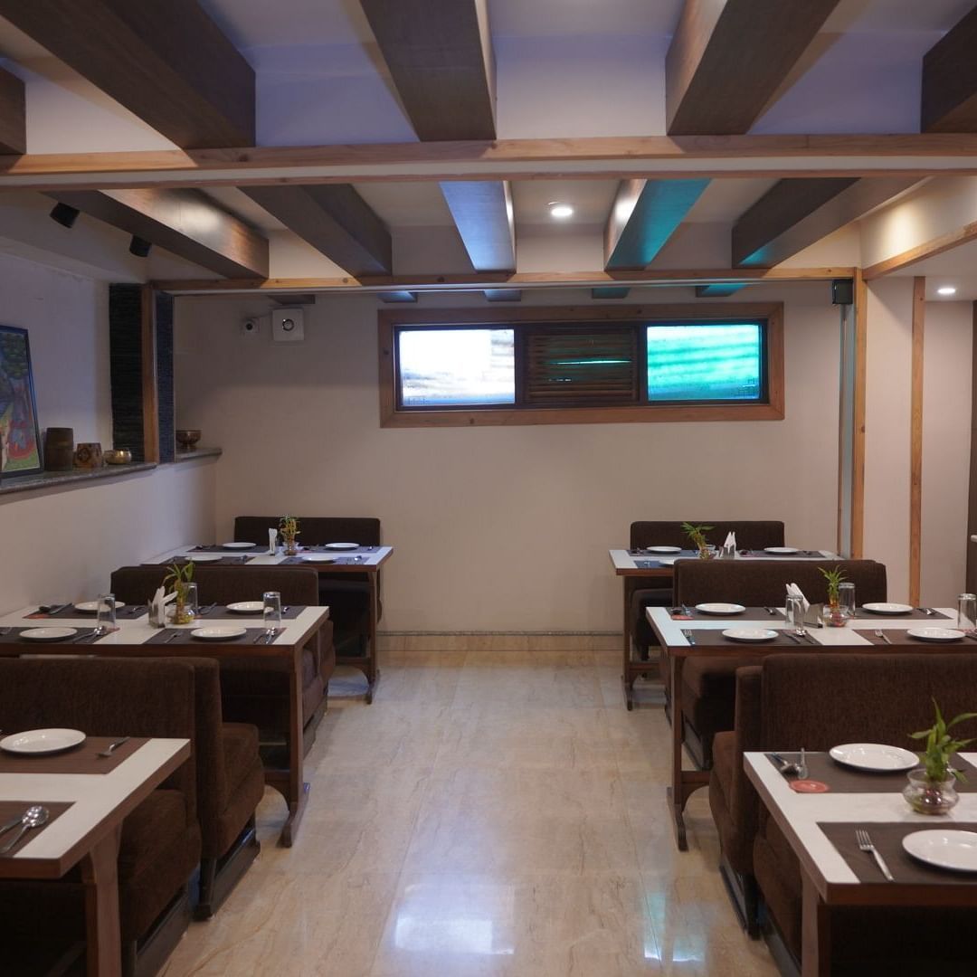 Blue Coriander restaurant with wooden interiors, six four-seating tables, cutlery placed neatly on each table and local interior additions placed on the sides.