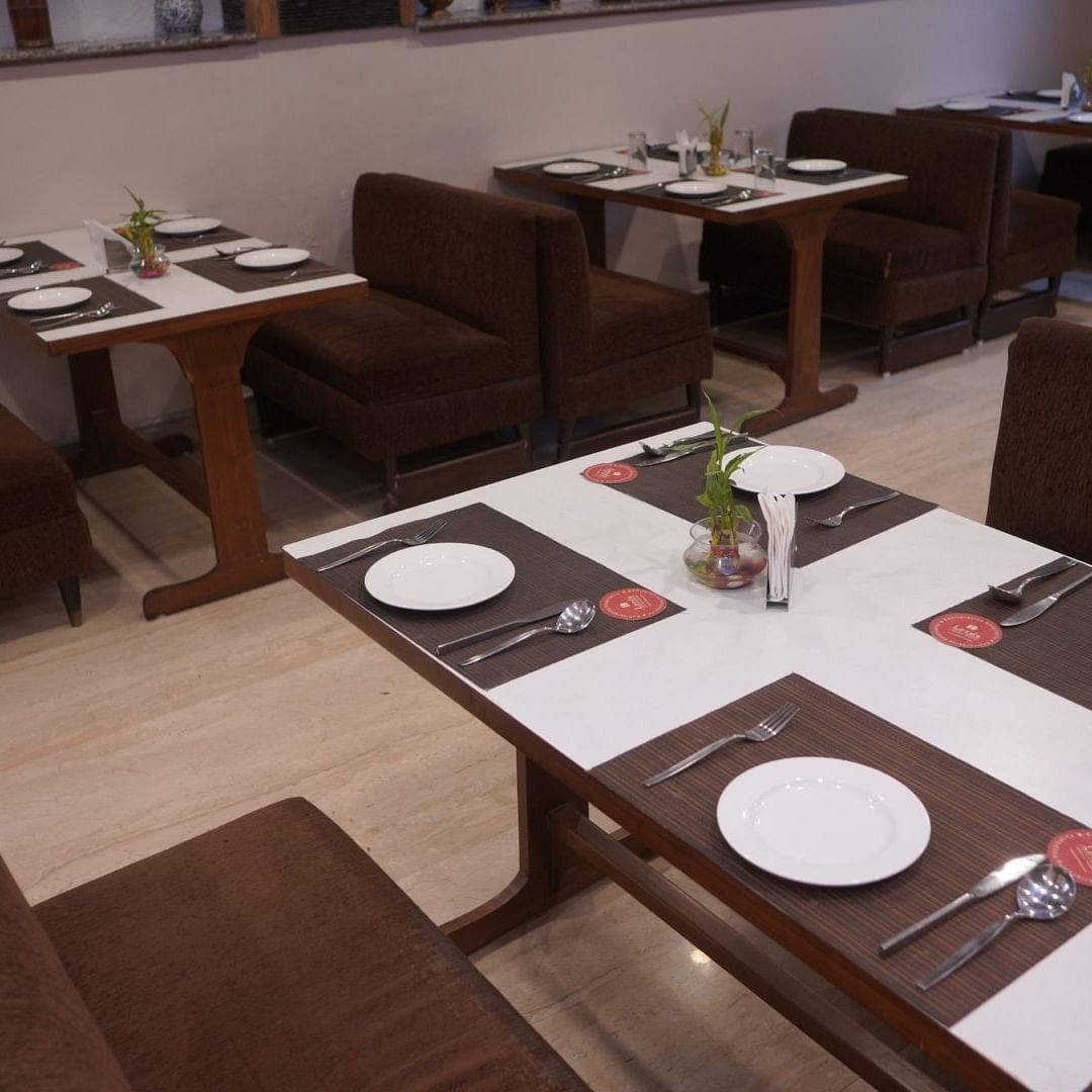 Blue Coriander restaurant at Orchid Lords Eco Inn, Gangtok features tables accompanied by two sofas each, with cutlery and plates neatly arranged on top.