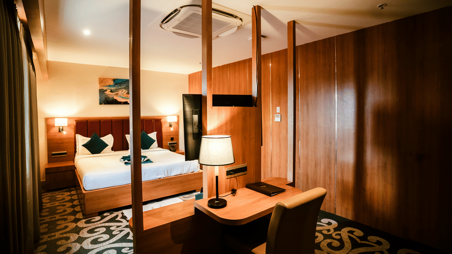 Executive Suite interior with a king bed, wooden partition, wall-mounted TV, writing desk and patterned carpet at Ilara Hotels & Spa, Tada.
