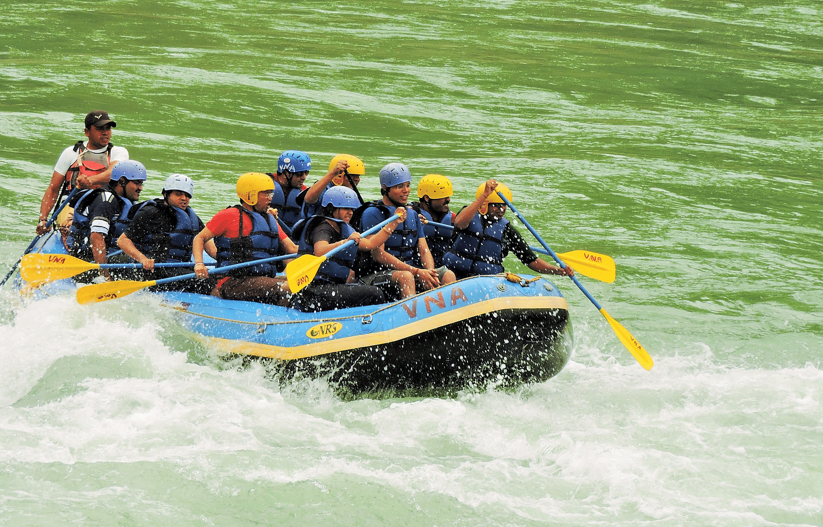 A group of people rafting on a single raft in a rushing river, splashing water around them. 