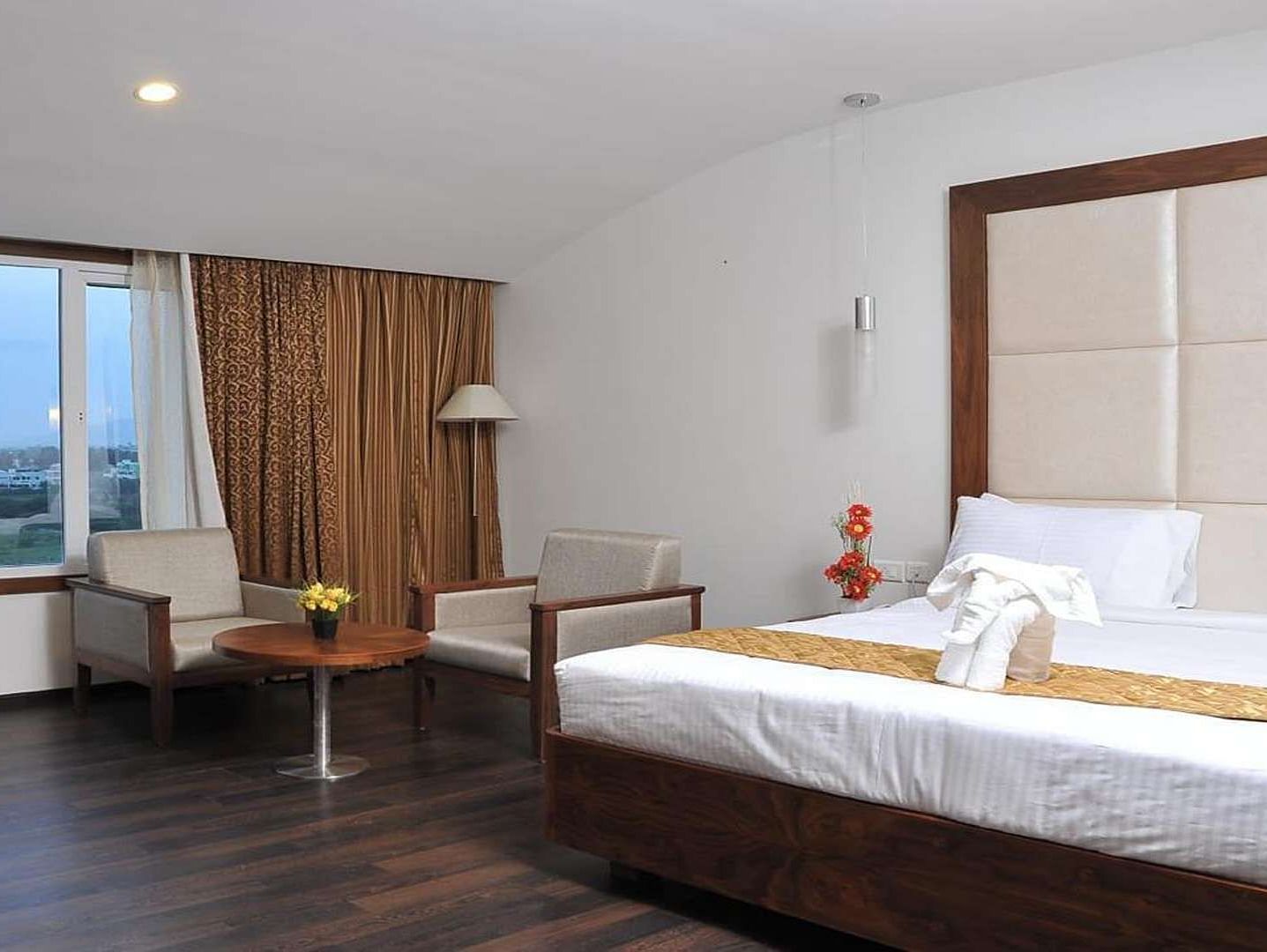 Executive Room with a king size bed, a chair, and a partially visible window at Dhanalaksmi Srinivasan Hotels, Perambalur