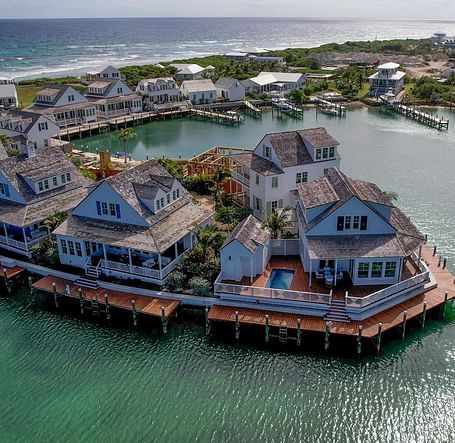 Drone view of villas and bungalows built over water with wooden decks, forming a semi-circle above a calm bay | Abaco Inn