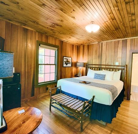 a wide angle shot of a bedroom with a modern looking table lamp kept on the round wooden coffee table - Historic Tapoco Lodge