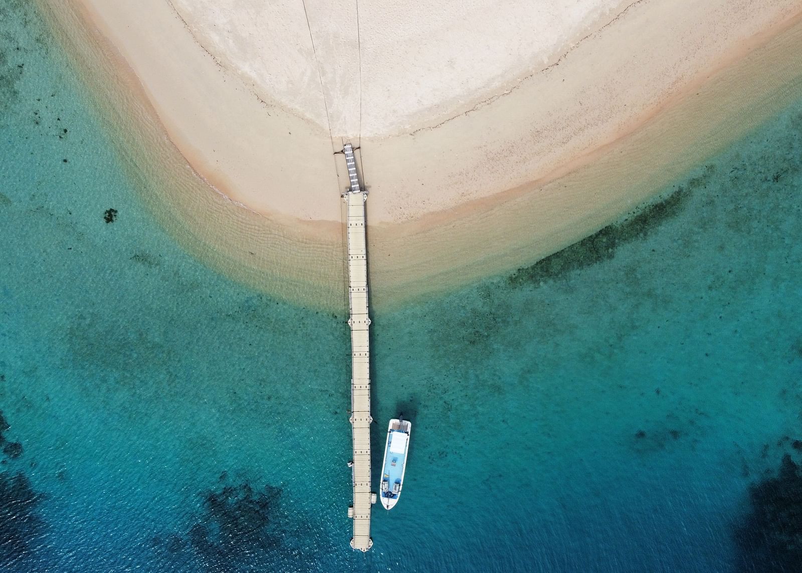 Aerial view of a white sand beach and boat docked at a pier near Flower Island Resort.
