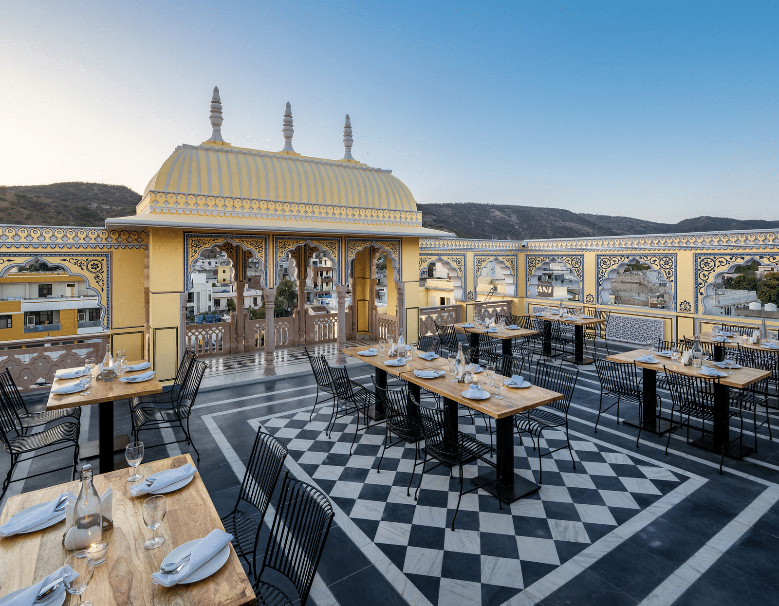 a roof top dining setup with beautiful views of the surrounding mountains and the early sunset - Brij Castle, Jaipur