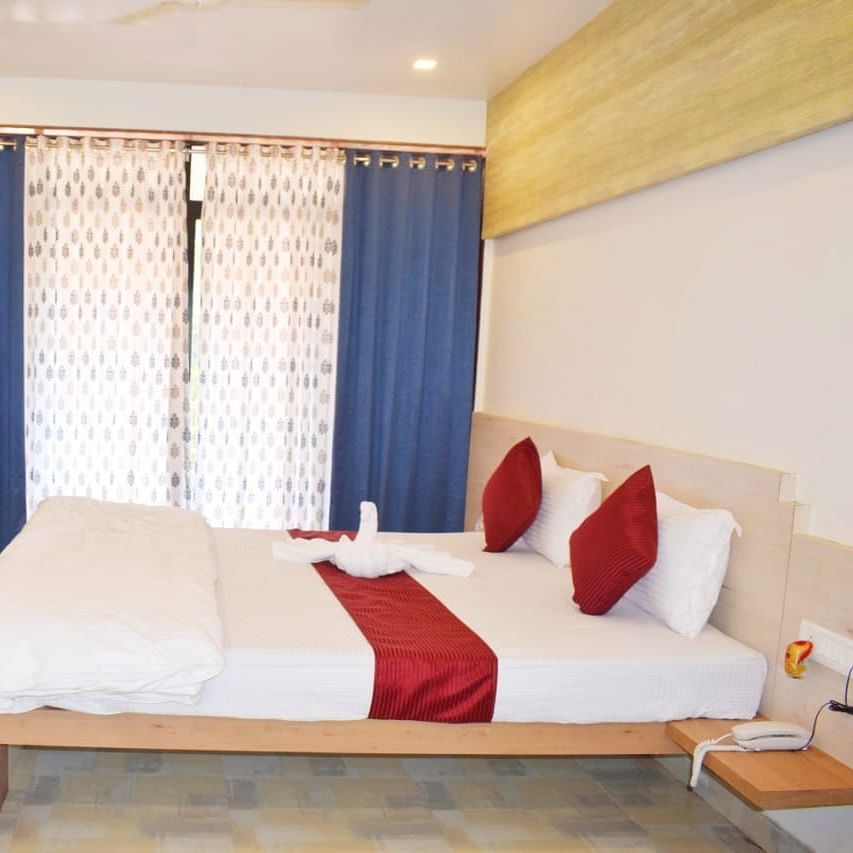 A side view of a spacious room with a large bed. Right opposite to it, there is a wall-mounted TV, and a large window with curtains fully covering it at SeaFort Beach Resort