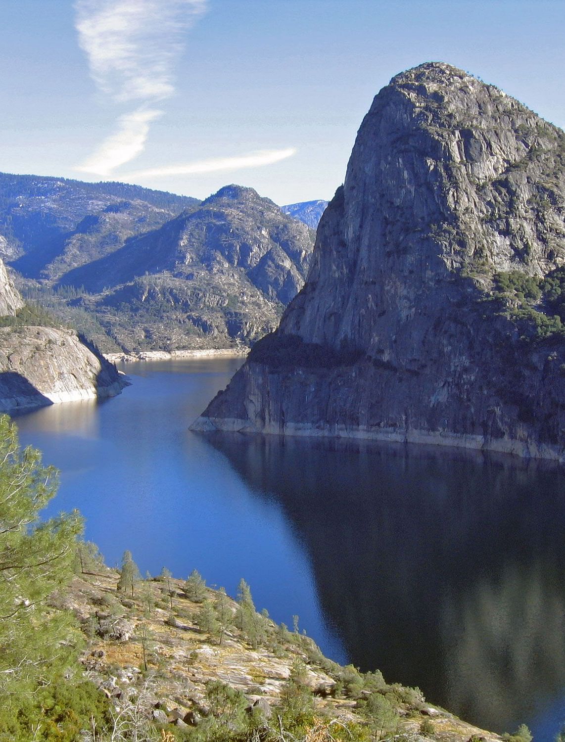 View of the Hetch Hetchy Reservoir, showcasing water flowing between majestic natural mountains under a bright, sunny sky
