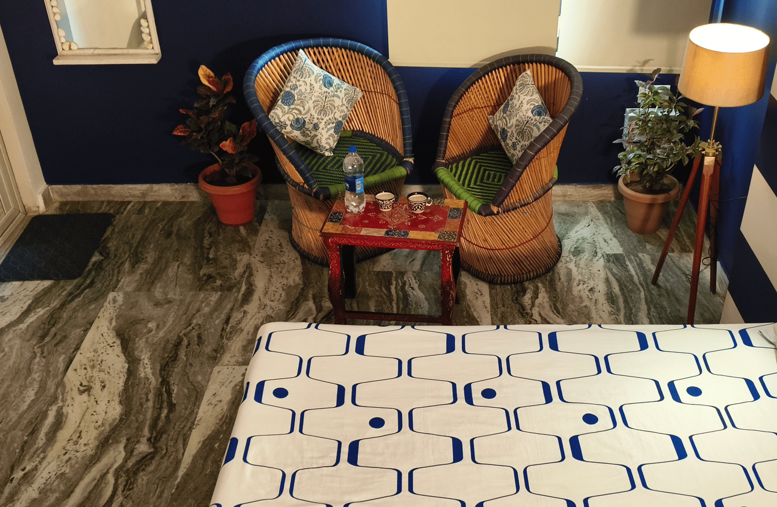 A bedroom with a bed, patterned bedspread, decorative pillows, chairs and plants in the corner at Jaypore360 Homestay - Best Rooms in Jaipur.