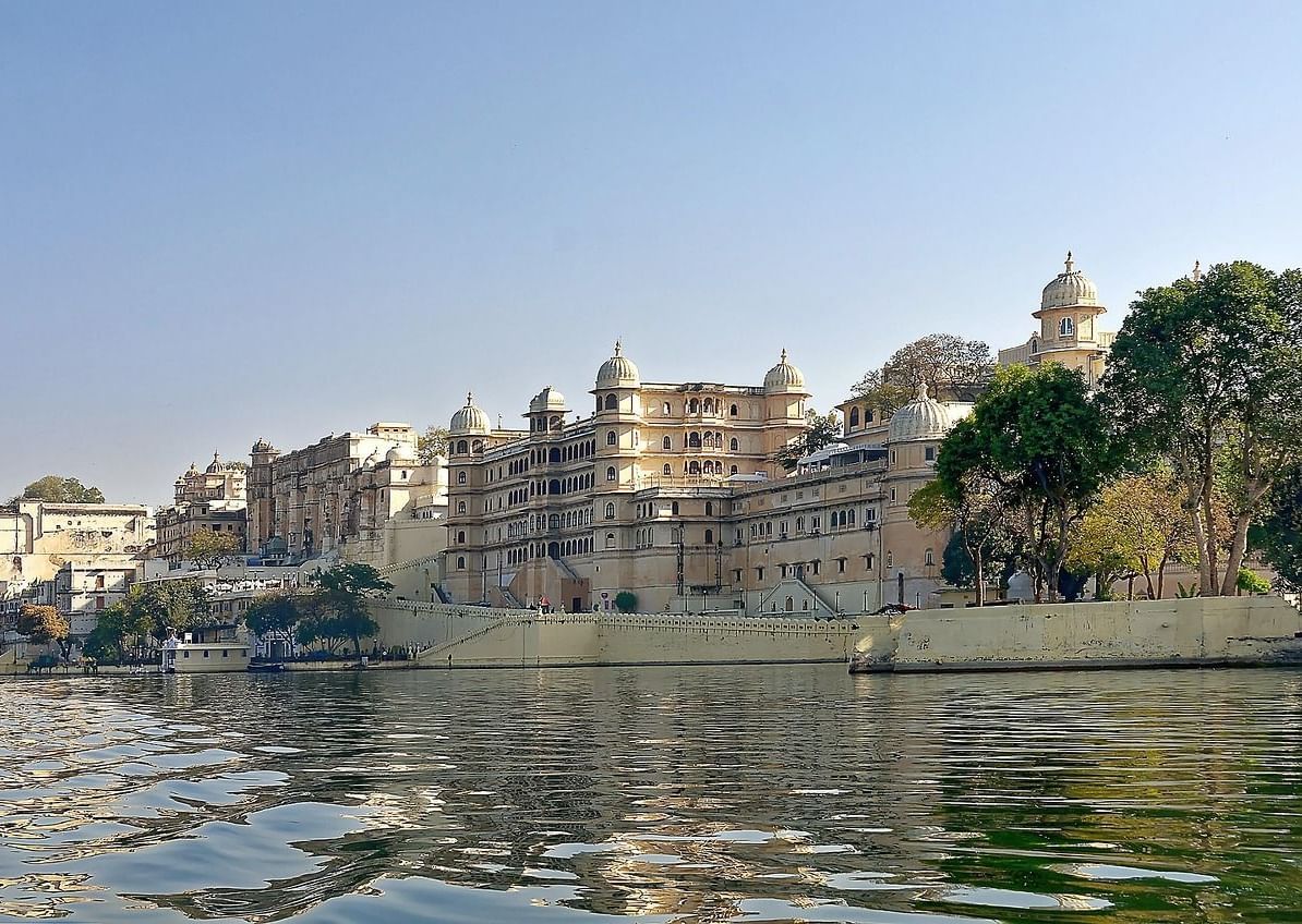 Jagdish Temple in Udaipur located beside a body of water, surrounded by trees.