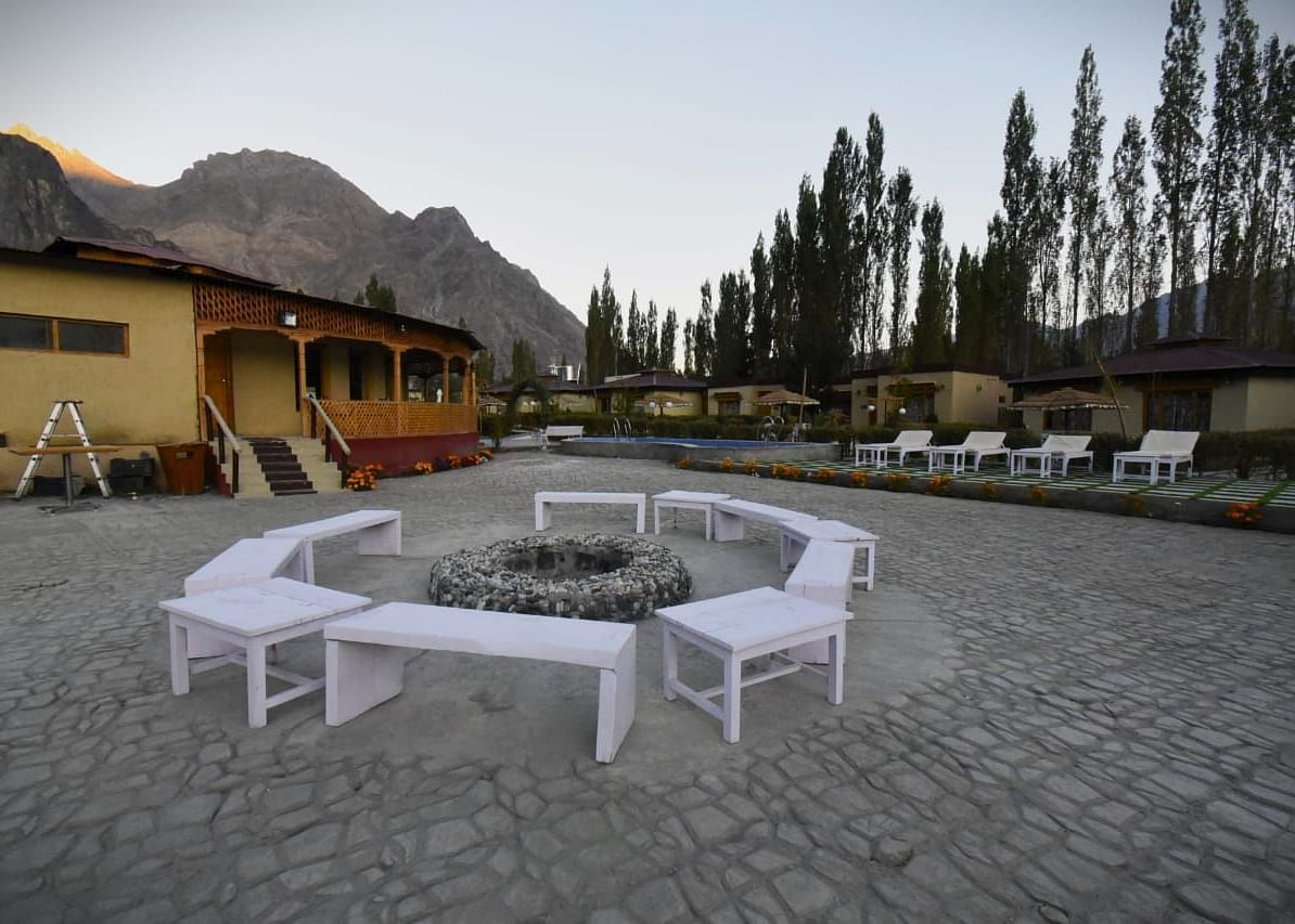 A bonfire setting with white seating area surrounded by buildings at White Sands Resort, Ladakh.