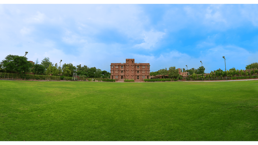 A large open green lawn stretching in front of a building under a blue sky at Garh Govind.