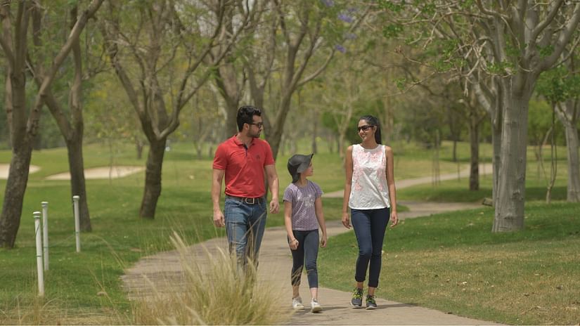 A family of three walking on the pathway with trees around - Karma Lakelands.