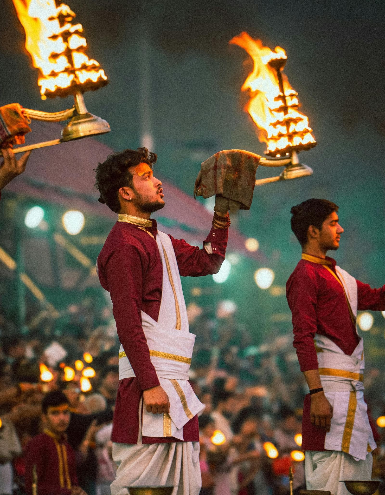 Several priests performing Ganga Arti with a heavy brass lamp dressed in ethnic wear.