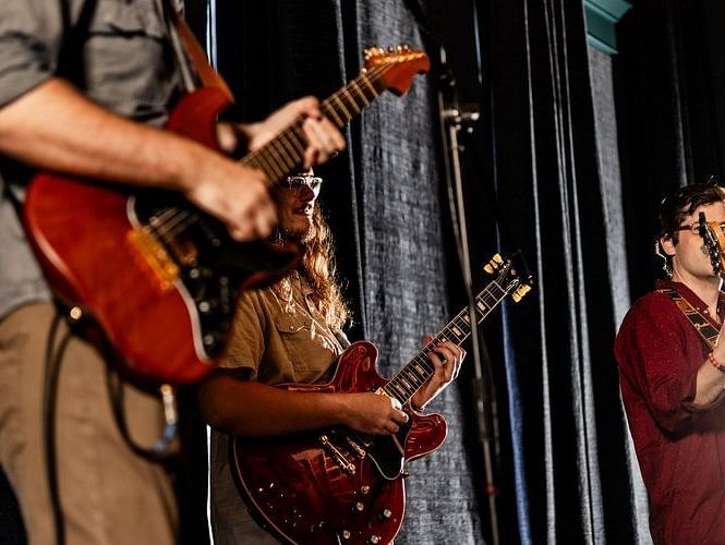 A musician playing a guitar while a singer performs on stage, creating an engaging entertainment experience.- The Grand Hotel & Ballroom, McKinney