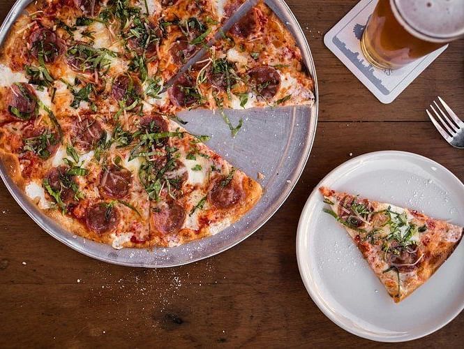 Top view of a Pizza on a big plate, pizza slice on a small saucer,a fork and a jar of a red condiment. 