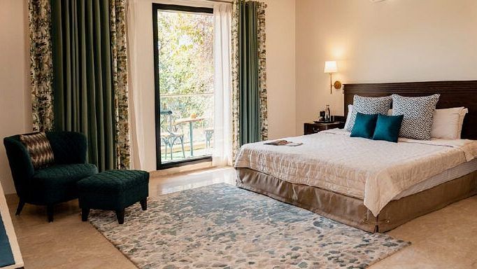Bedroom with a bed, dark headboard, armchair, and curtains drawn open at Karma Chalets.