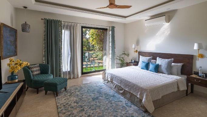 Bright bedroom with a double bed, armchairs, and natural light from large windows at Karma Chalets.