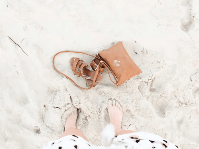 Sandals, a purse, and other accessories lie on white sand.