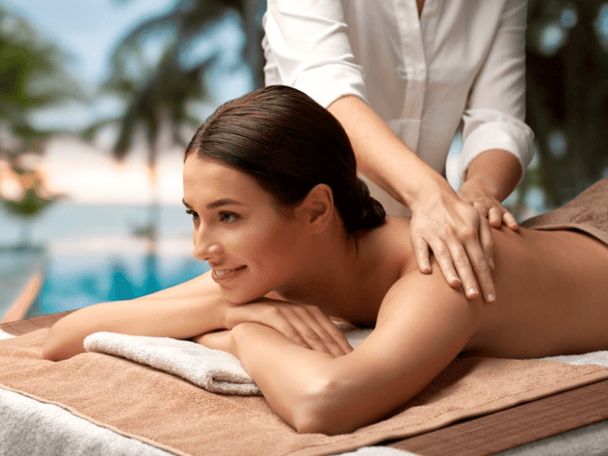  A woman receiving a back massage outdoors by a swimming pool.