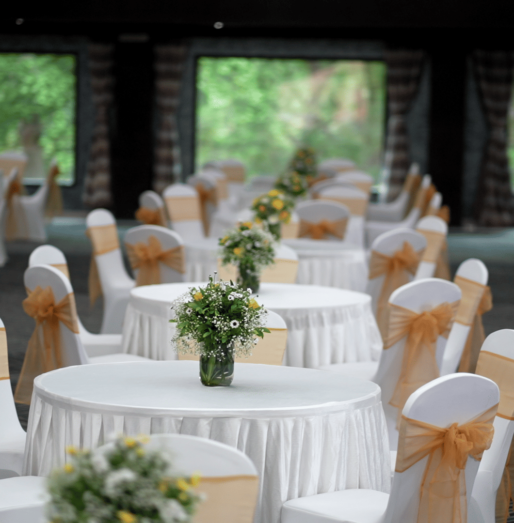 Banquet hall setup with round tables, white and gold chair covers, and floral centrepieces at Narayani Heights Hotel & Resorts, Ahmedabad.