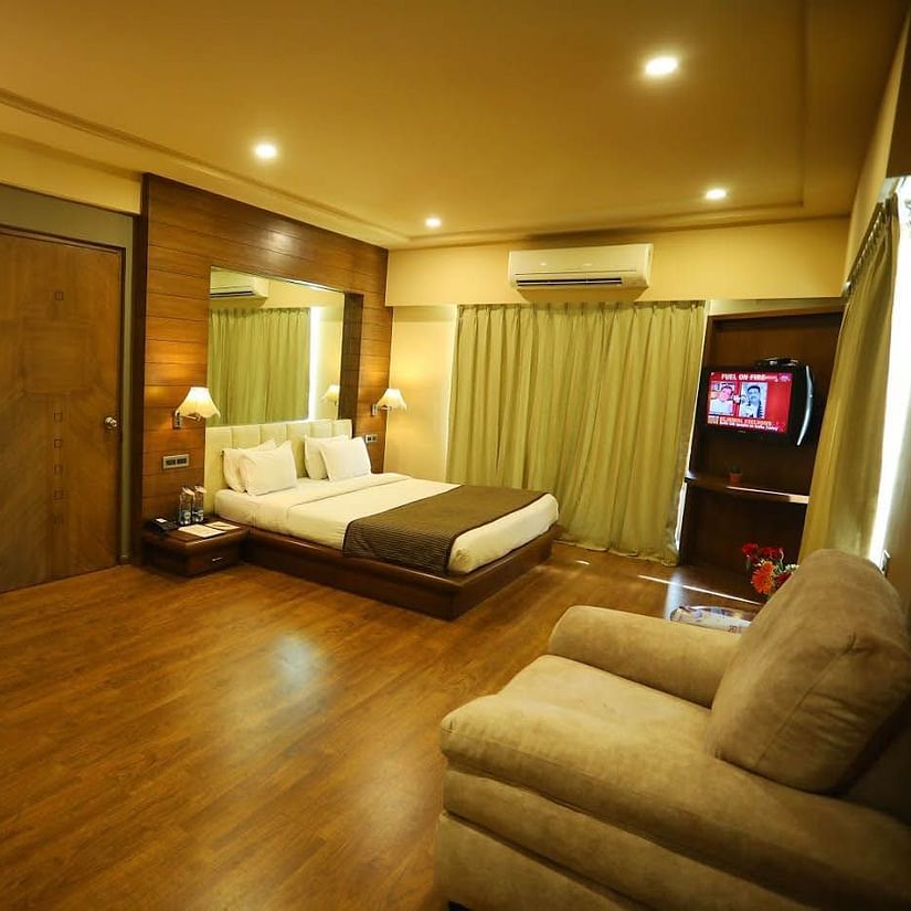 A comfortable hotel room features a bed, seating, a desk, and a television. The room has ample space and natural light - Renest Gandhidham