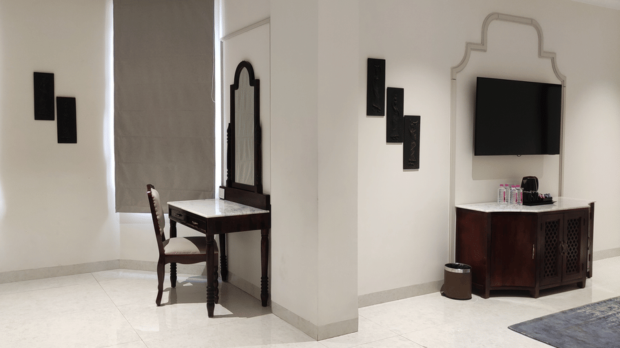 A view of a room at Anant Mahal, Jaipur with a wall mounted television, black decorative wall accents,a mirror, a wooden dressing table and chair.