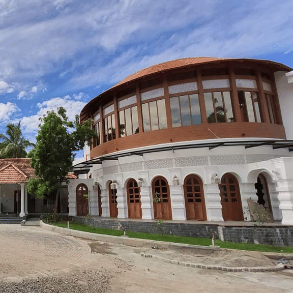 A large circular building with tall arches and a curved facade, surrounded by greenery under a blue sky.
