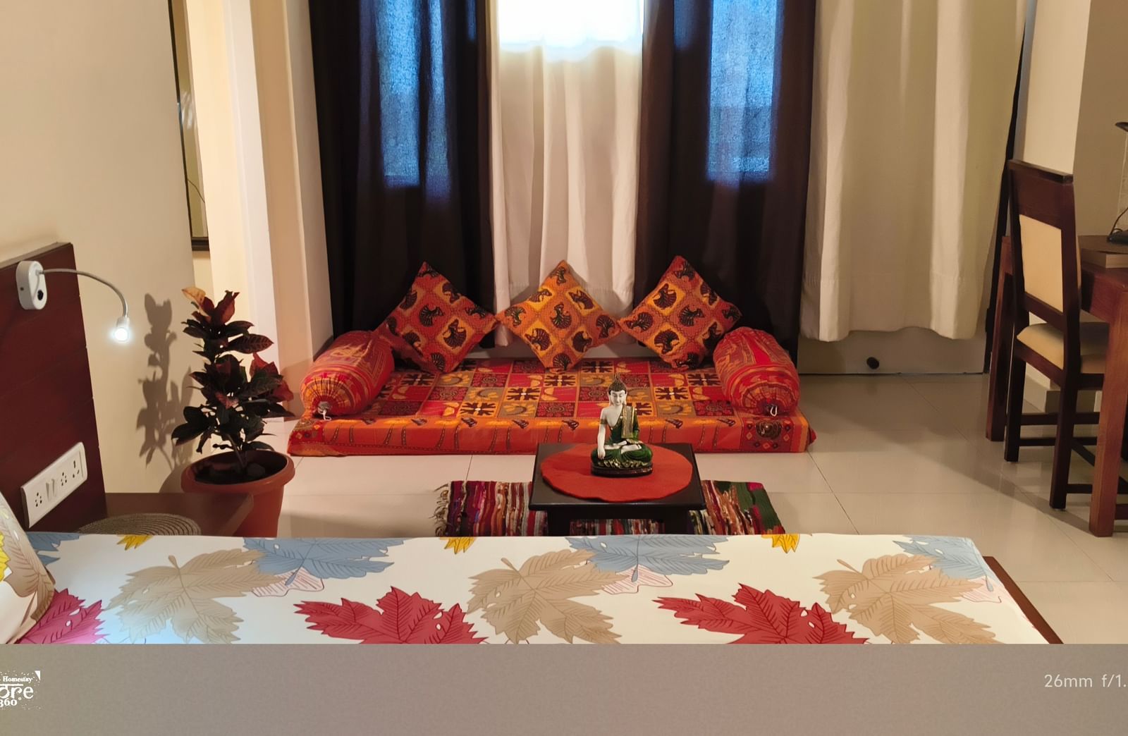 A cosy bedroom with a double bed, seating area with cushions, curtains and a wooden table at Jaypore360 Homestay - Best Homestays in Jaipur.