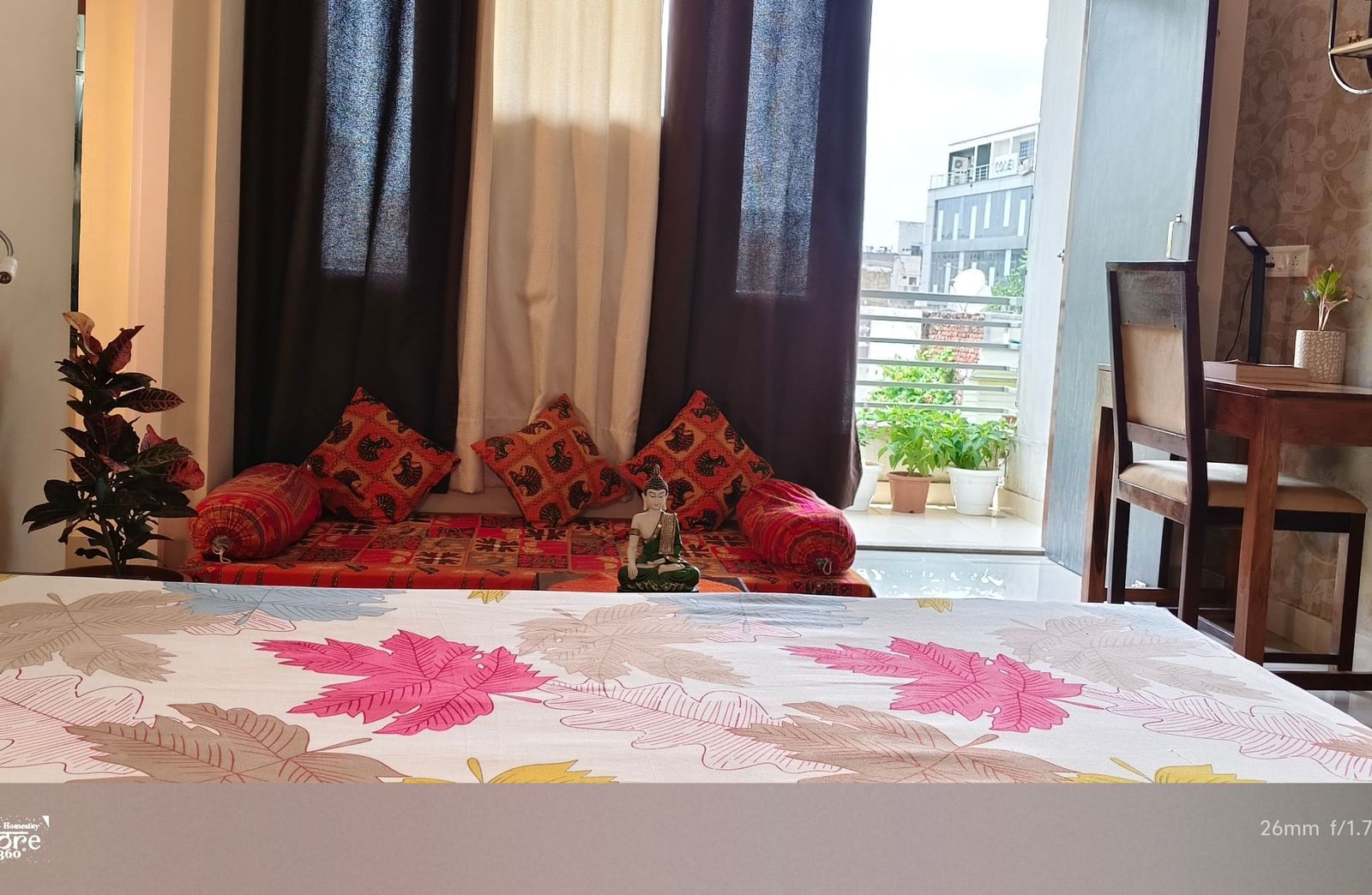 A well-lit bedroom with a large bed, patterned bedding, window curtains and chairs near the balcony at Jaypore360 Homestay - Best Homestays in Jaipur.