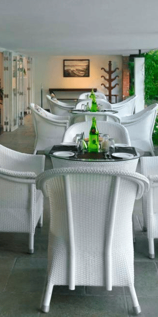 Modern covered patio with bar and white tables and chairs at Amanvana Spa Resort Coorg overlooking lush green surroundings.