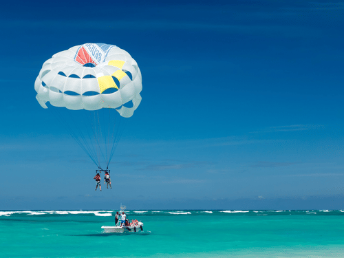 Two people parasailing above turquoise waters while being towed by a speedboat during a water sports adventure in Goa.