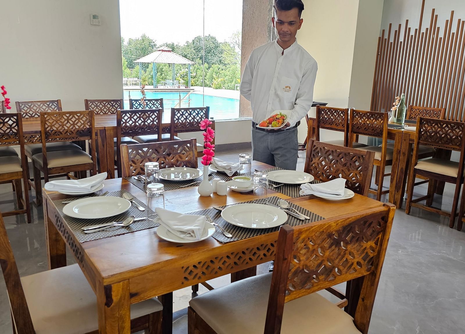 A man in a light-coloured shirt stands in a restaurant, possibly a waiter or staff member where tables and chairs are visible - Bamboo Saa Mulberry Resort, Pushkar
