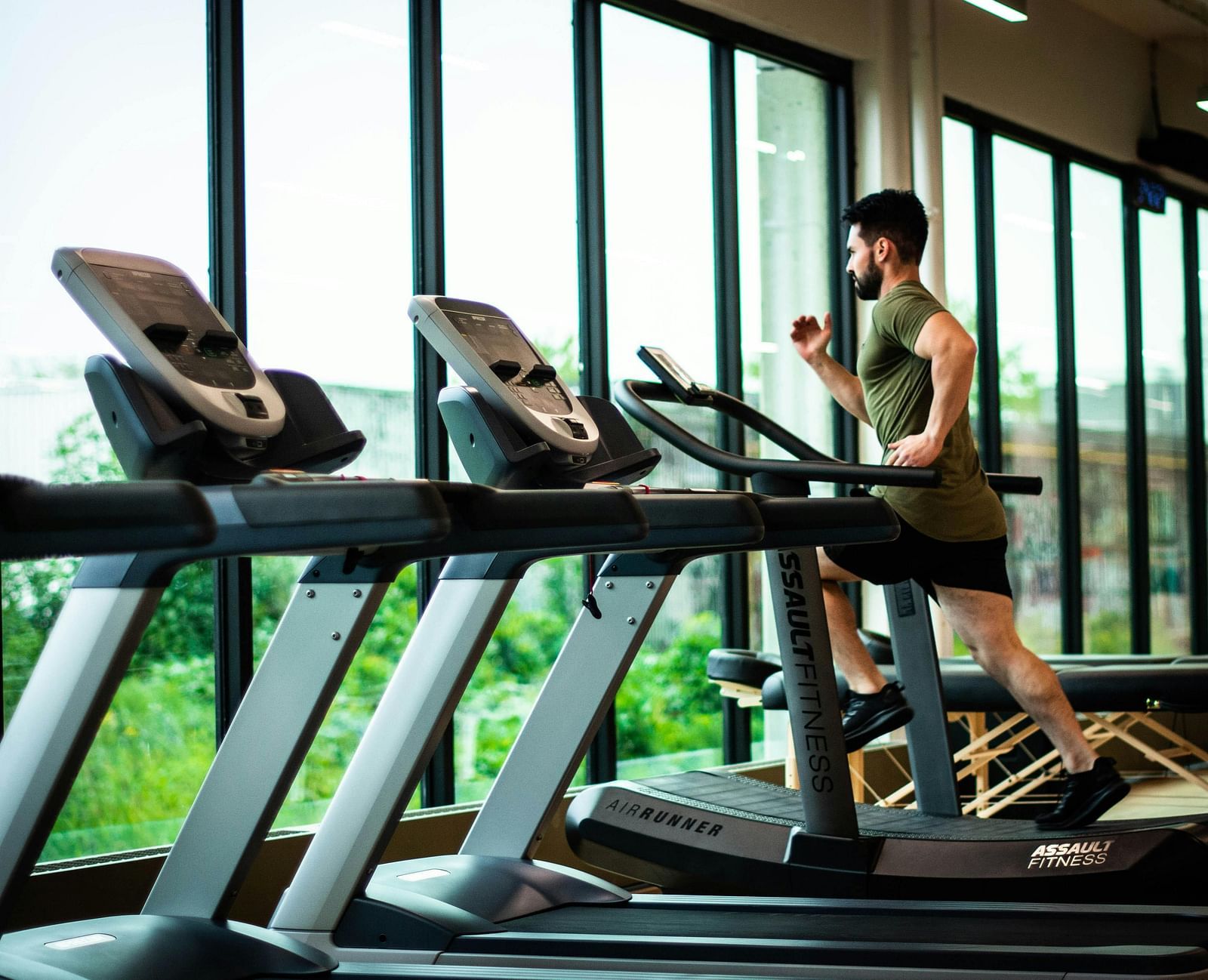 A man running on a treadmill with lush green views outside the huge glass windows.