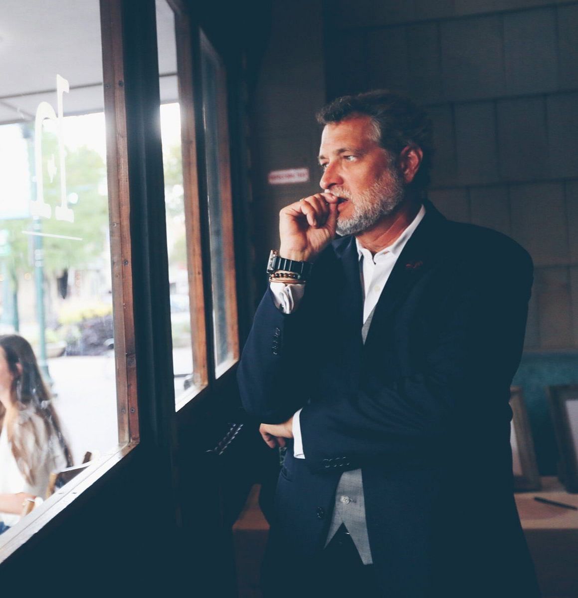  A professional man in a suit talking on the phone by a window, appearing focused and engaged in conversation.