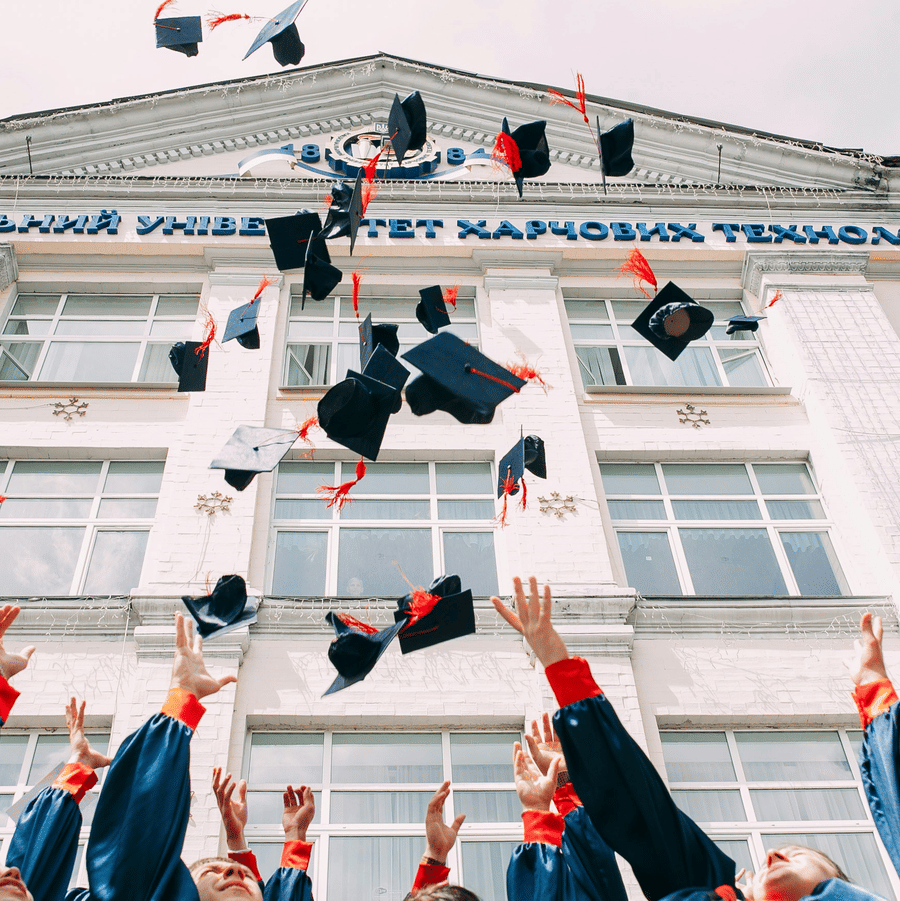 Students in gowns tossing their graduation caps in front of a university building