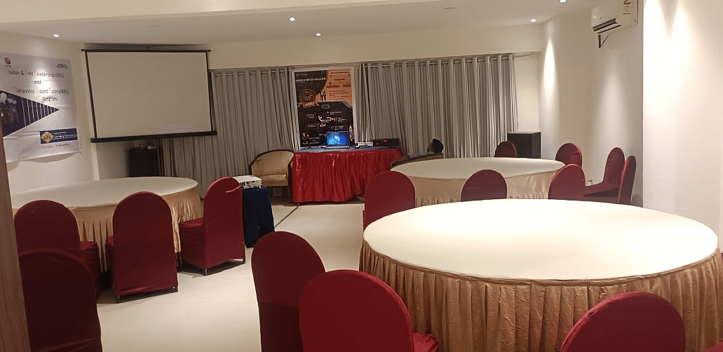 Professional banquet hall at Lords Eco Inn Dahej with round tables, burgundy chairs, and presentation screen for events and conferences