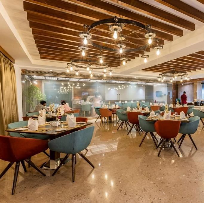 Warmly lit dining area at Rang Lords Inn, with a wooden beamed ceiling, modern chairs, and set tables