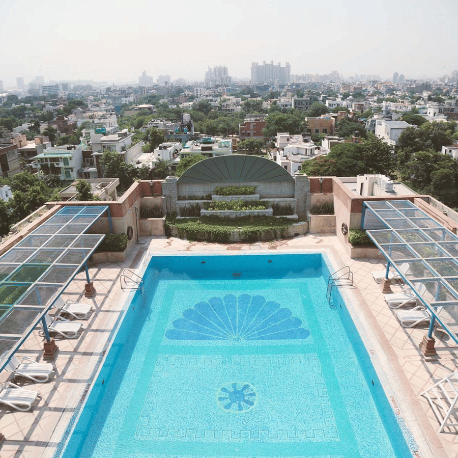 Rooftop swimming pool at The Bristol Hotel, Gurgaon with a mosaic fan pattern on the pool floor, sun loungers on either side, and city skyline beyond.