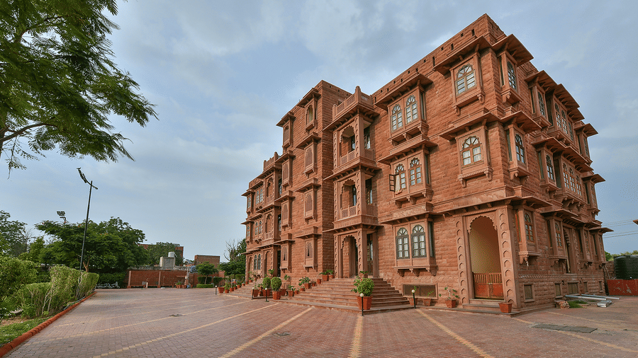 A multi-storey stone building at Garh Govind standing next to a paved courtyard under a cloudy sky with trees to the left.